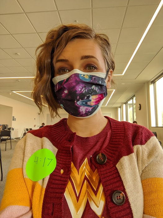 Woman wearing a surgical mask, sitting inside a large waiting room.